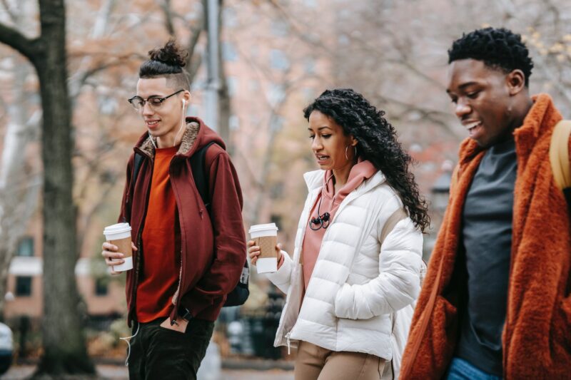 group of multiethnic students walking on street with coffee cups
